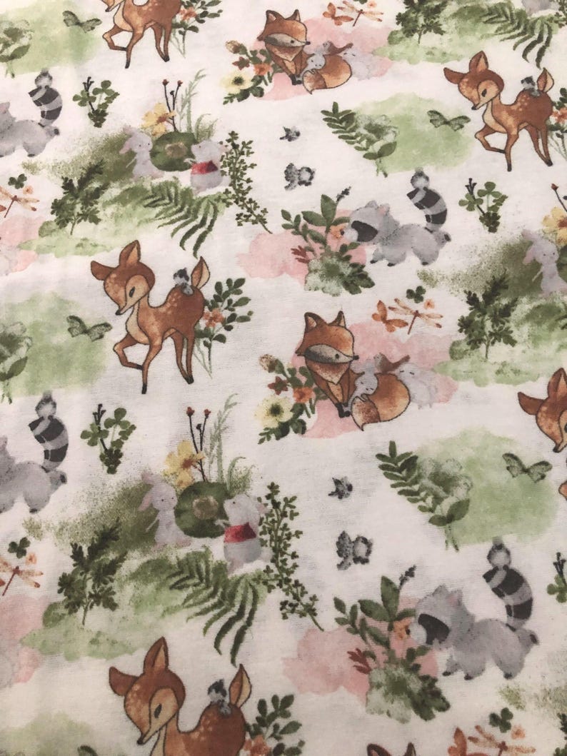 May include: White fabric with a repeating pattern of woodland animals and floral elements. The design features deer, foxes, raccoons, and rabbits, along with flowers, butterflies, and greenery in soft colors.