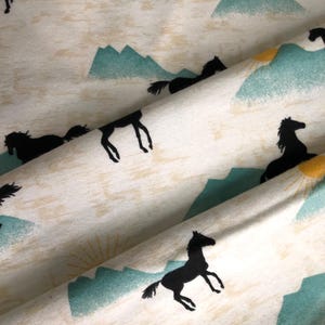 May include: Cream-colored fabric with a repeating pattern of black horses, teal mountains, and yellow suns. The horses are in various poses, some galloping, others standing. The design has a rustic, outdoorsy feel.