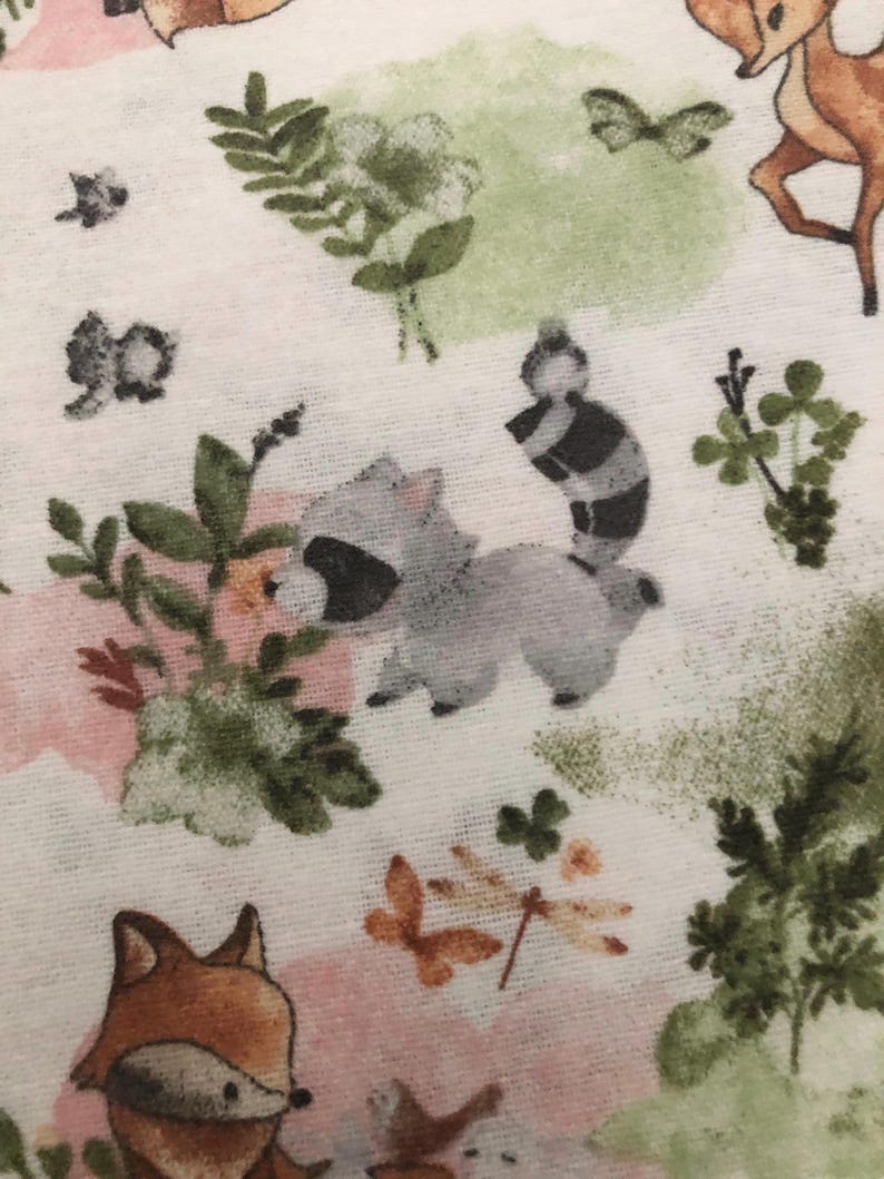 May include: White fabric with a repeating pattern of woodland creatures and floral elements. The design includes raccoons, foxes, deer, butterflies, and green foliage, set against soft pink and green watercolor-style backgrounds.