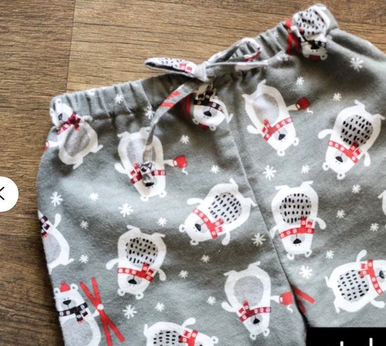 May include: Gray pajama pants with a repeating pattern of white polar bears wearing red scarves and hats, and red mittens. The pants have a drawstring waist and white snowflakes scattered throughout the design.
