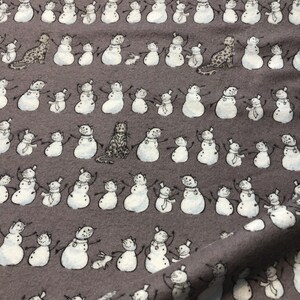 K&ouml;nnte beinhalten: Grauer Stoff mit einem sich wiederholenden Muster aus Schneem&auml;nnern und Tierfiguren. Die Schneem&auml;nner sind wei&szlig; mit schwarzen Details, tragen H&uuml;te und Schals. Zu den Tieren geh&ouml;ren Katzen und Kaninchen. Der Stoff hat ein weiches, strukturiertes Aussehen.