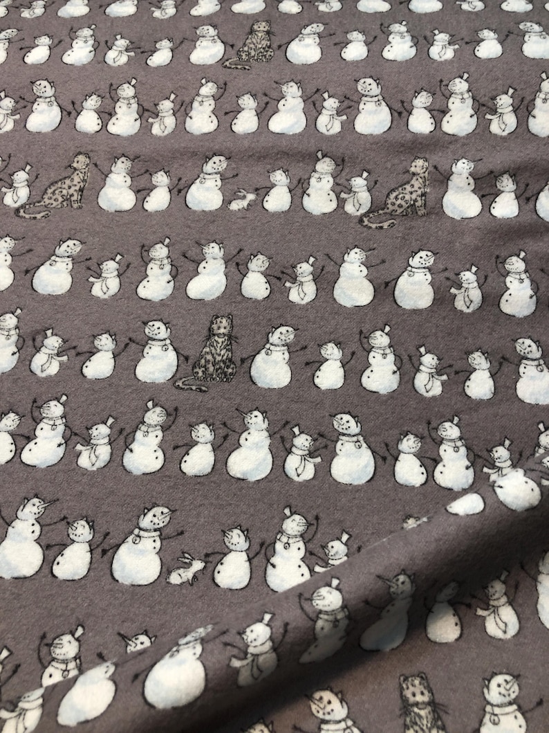 K&ouml;nnte beinhalten: Grauer Stoff mit einem sich wiederholenden Muster aus Schneem&auml;nnern und Tierfiguren. Die Schneem&auml;nner sind wei&szlig; mit schwarzen Details, tragen H&uuml;te und Schals. Zu den Tieren geh&ouml;ren Katzen und Kaninchen. Der Stoff hat ein weiches, strukturiertes Aussehen.