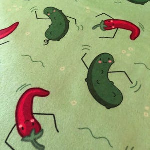 May include: Green fabric with a repeating pattern of green pickles and red chilli peppers. The pickles and peppers have cartoon faces and are dancing.