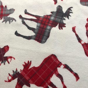 May include: White fabric featuring a repeating pattern of moose silhouettes in red and grey plaid. The moose are in various poses, creating a dynamic design. The fabric appears to be a cotton or linen blend.