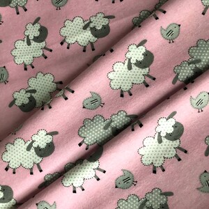 May include: Pink fabric with a repeating pattern of white sheep with gray faces and bodies, and small gray birds. The sheep have dotted bodies and are outlined with a dotted stitch. The birds have two stripes on their bodies.
