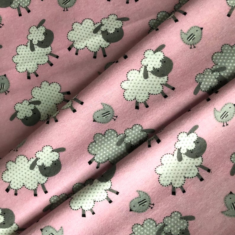 May include: Pink fabric with a repeating pattern of white sheep with gray faces and bodies, and small gray birds. The sheep have dotted bodies and are outlined with a dotted stitch. The birds have two stripes on their bodies.