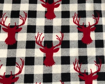 Könnte beinhalten: Ein Stoff mit einem sich wiederholenden Muster aus roten Hirschköpfen auf einem schwarz-weißen Büffel-Plaid-Hintergrund. Die Hirschköpfe sind silhouettenartig und haben große Geweihe. Das Muster ist gleichmäßig über den Stoff verteilt.
