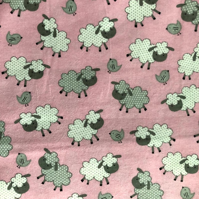 May include: Pink fabric with a repeating pattern of white sheep with gray polka dots and gray faces, interspersed with small gray birds. The sheep have a fluffy appearance, and the birds have simple, stylized designs.