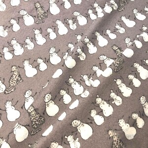 K&ouml;nnte beinhalten: Ein grauer Stoff mit einem sich wiederholenden Muster aus wei&szlig;en Schneem&auml;nnern und Leopardenfiguren. Die Schneem&auml;nner haben schwarze Arme und Karottennasen. Der Stoff hat ein weiches, leicht strukturiertes Aussehen.