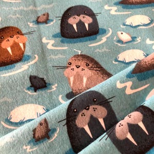 Może przedstawiać: Niebieski materiał z powtarzającym się wzorem brązowych, szarych i czarnych morsa z białymi kłami. Morsy pływają w niebieskiej wodzie z białymi falami i kry.