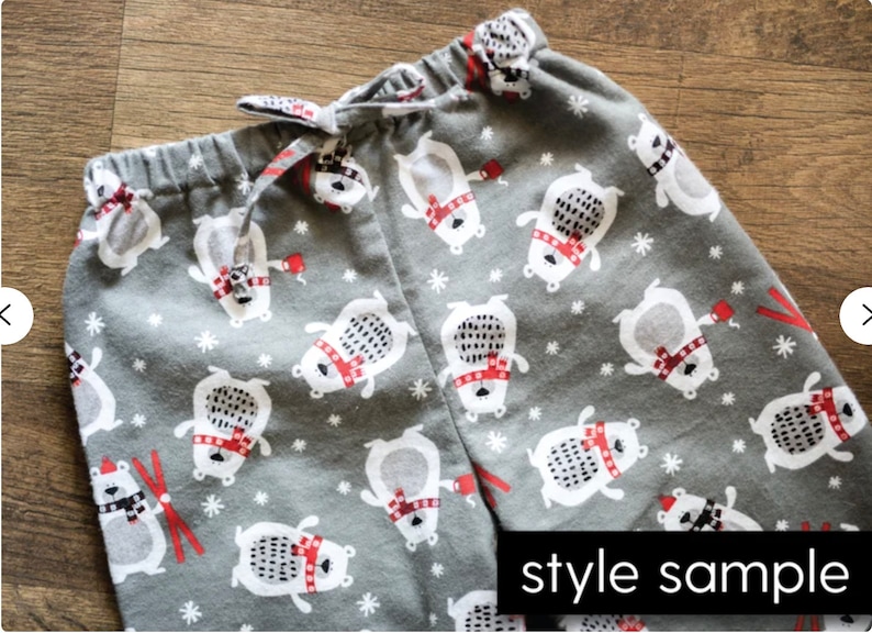 以下が含まれることがあります： 白いホッキョクグマのプリントが施されたグレーのパジャマパンツ。クマは赤いマフラーを巻いて赤いマグカップを持っています。パンツには白い雪の結晶模様と赤いスキーの棒があります。