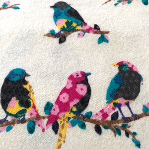 May include: A white fabric with a repeating pattern of colorful birds perched on branches. The birds have black bodies, yellow beaks, and pink and blue accents. The branches are brown with green leaves.