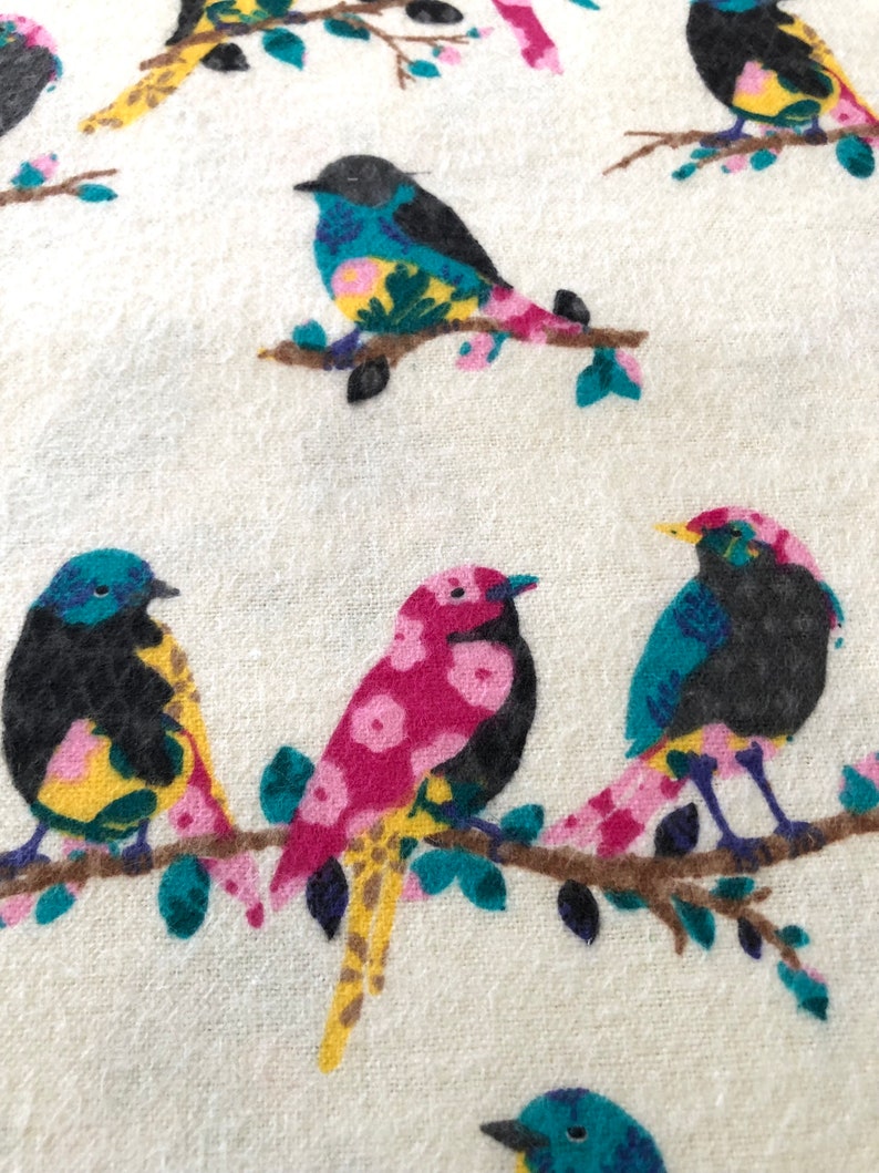 May include: A white fabric with a repeating pattern of colorful birds perched on branches. The birds have black bodies, yellow beaks, and pink and blue accents. The branches are brown with green leaves.