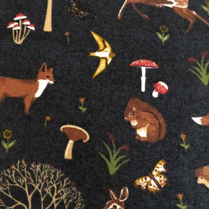 Pode incluir: Um tecido azul escuro com um padr&atilde;o repetitivo de animais da floresta, incluindo veados, raposas, esquilos, p&aacute;ssaros, cogumelos e &aacute;rvores. O tecido tem uma textura macia e felpuda.