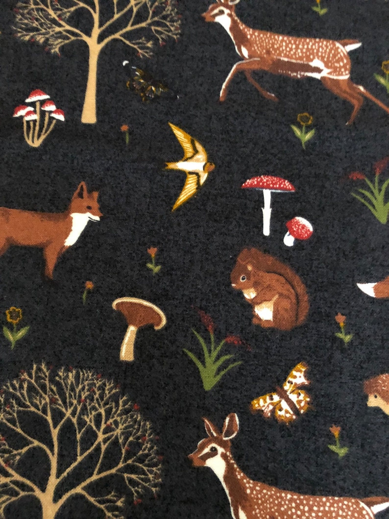 Pode incluir: Um tecido azul escuro com um padr&atilde;o repetitivo de animais da floresta, incluindo veados, raposas, esquilos, p&aacute;ssaros, cogumelos e &aacute;rvores. O tecido tem uma textura macia e felpuda.