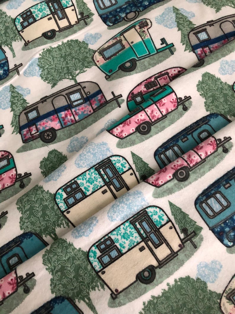 May include: White fabric with a repeating pattern of vintage camper trailers in teal, pink, and blue, adorned with floral and geometric designs. The design includes green trees and blue clouds, creating a whimsical, outdoorsy theme.