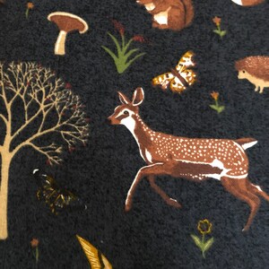 Pode incluir: Um tecido azul escuro com um padr&atilde;o repetitivo de animais da floresta, cogumelos e plantas. Os animais incluem um veado, um esquilo, um ouri&ccedil;o e um p&aacute;ssaro. Os cogumelos s&atilde;o castanhos e vermelhos. As plantas s&atilde;o verdes e castanhas.