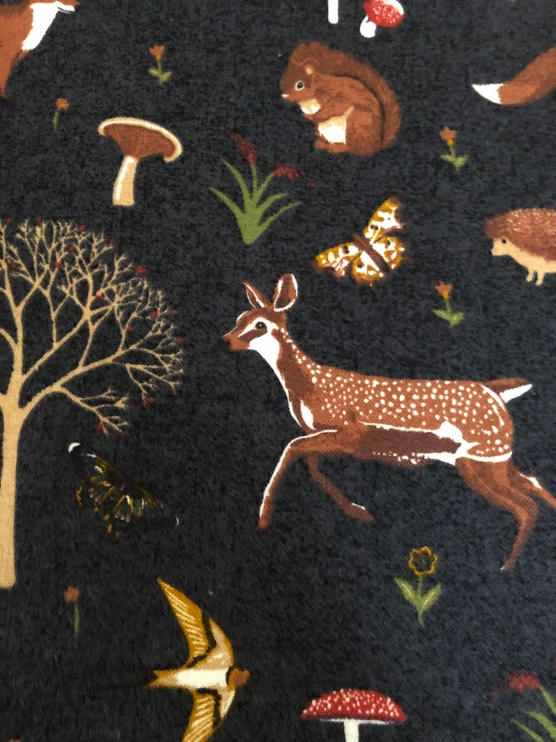 Pode incluir: Um tecido azul escuro com um padr&atilde;o repetitivo de animais da floresta, cogumelos e plantas. Os animais incluem um veado, um esquilo, um ouri&ccedil;o e um p&aacute;ssaro. Os cogumelos s&atilde;o castanhos e vermelhos. As plantas s&atilde;o verdes e castanhas.