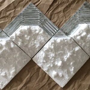 May include: Close-up of five white textured tiles with a silver border. The tiles are arranged in a staggered pattern.