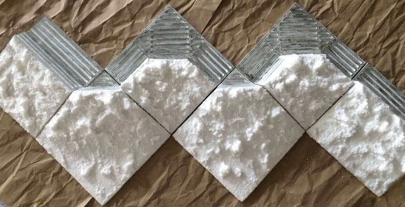 May include: Close-up of five white textured tiles with a silver border. The tiles are arranged in a staggered pattern.