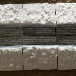 May include: Six white concrete blocks with a rough, textured surface. The blocks are arranged in two rows of three, with the top row slightly offset from the bottom row. The blocks are a light gray color and have a slightly uneven surface.