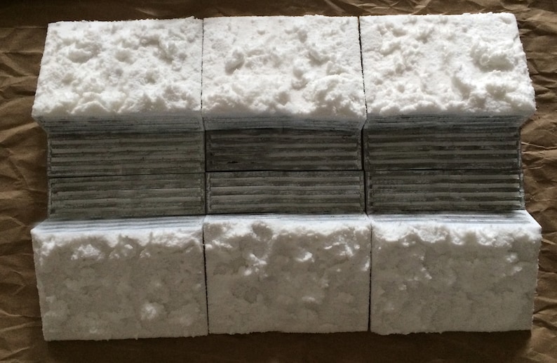May include: Six white concrete blocks with a rough, textured surface. The blocks are arranged in two rows of three, with the top row slightly offset from the bottom row. The blocks are a light gray color and have a slightly uneven surface.
