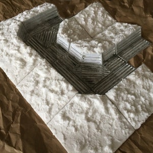 May include: A white, textured, foam-like material is used to create a model of a snowy landscape. The material is arranged in a series of squares and rectangles, with a raised, textured surface that resembles snow.