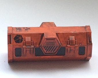May include: An orange-colored, rectangular box with a hexagonal vent and black details. The box has a textured surface and appears to be made of plastic.