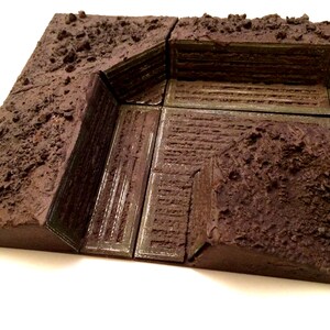 Pode incluir: Um modelo texturizado marrom e cinza de uma trincheira ou bunker com uma borda elevada e um piso texturizado.
