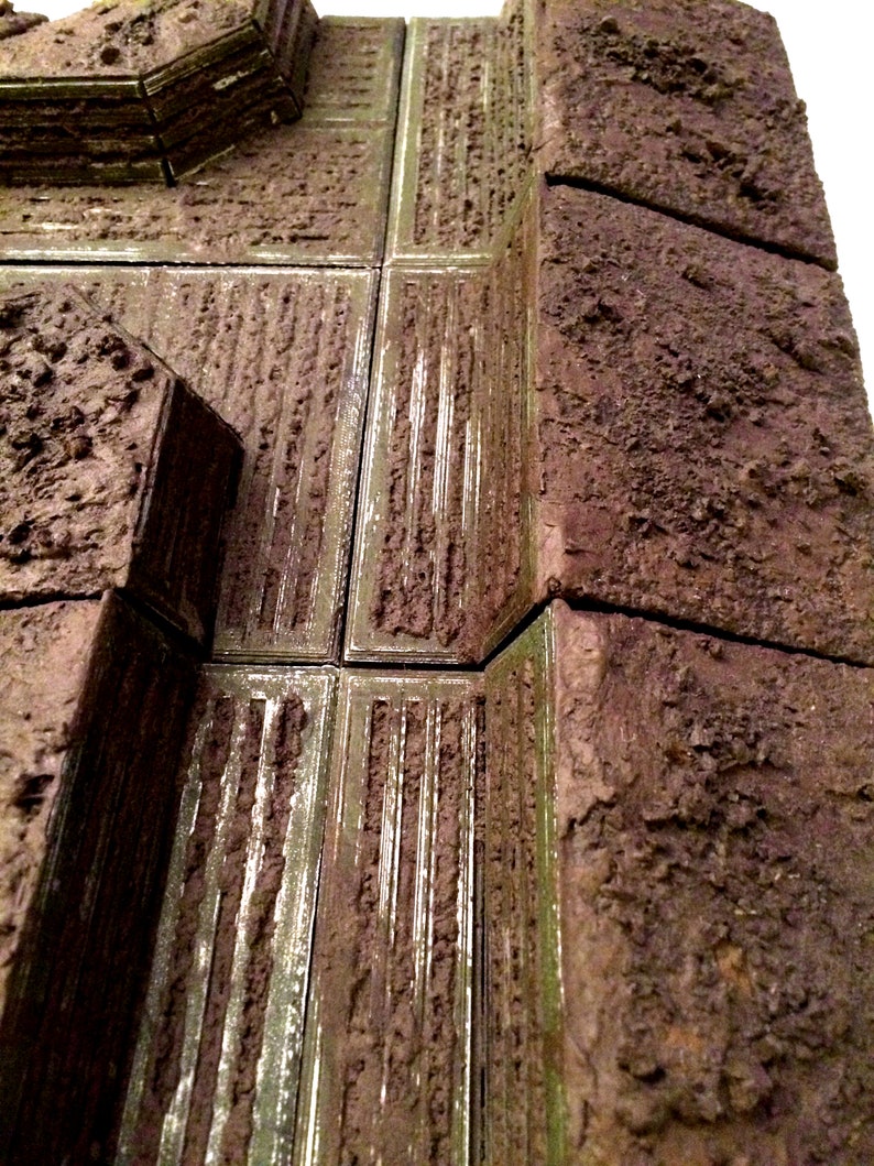 Pode incluir: Um close-up de um modelo texturizado de um edif&iacute;cio marrom e verde com uma abertura retangular. O modelo &eacute; feito de um material que se assemelha a pedra ou concreto.