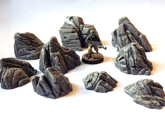 May include: A set of nine gray, textured, rocky terrain pieces for tabletop gaming or model building. The rocks are various sizes and shapes, with some having a more jagged appearance than others.