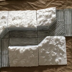 May include: A set of eight white textured tiles with a gray textured center section. The tiles are arranged in a rectangular shape, with the gray center section forming a square.