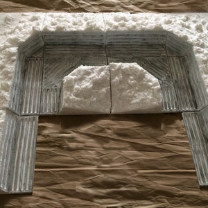 May include: A white foam model of a snow-covered archway, made of multiple pieces. The archway is made of a textured material that resembles stone or concrete.
