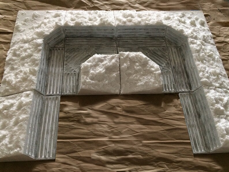 May include: A white foam model of a snow-covered archway, made of multiple pieces. The archway is made of a textured material that resembles stone or concrete.