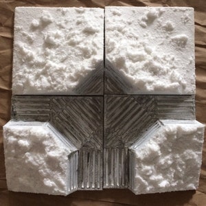 May include: A model of a building with a white snow-covered roof and a silver metal base. The building is made of four square sections, each with a different texture.