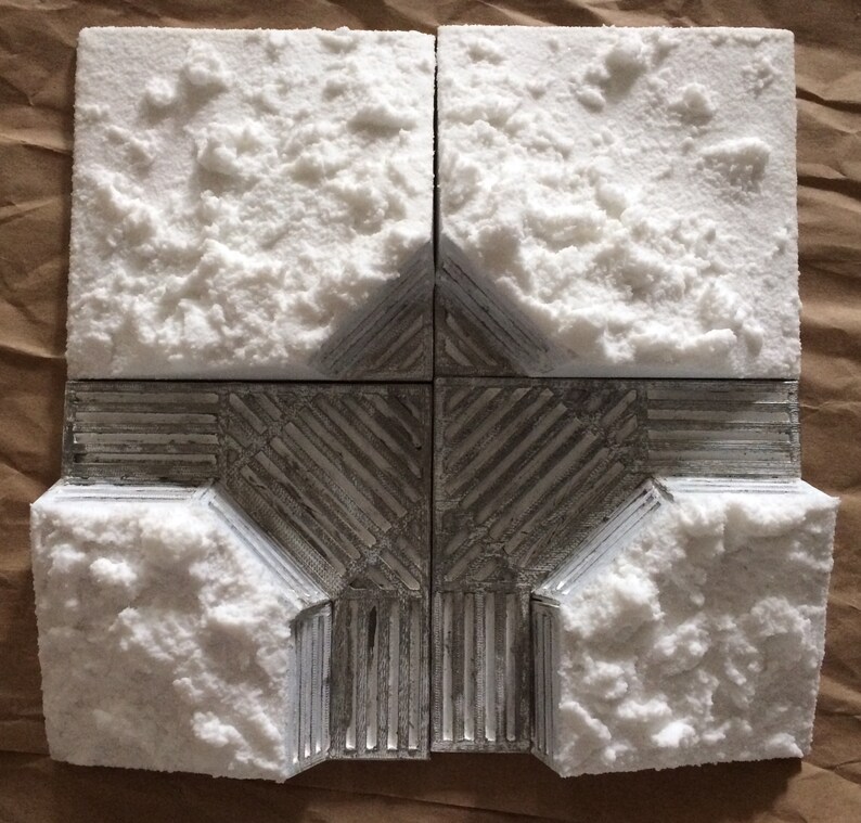 May include: A model of a building with a white snow-covered roof and a silver metal base. The building is made of four square sections, each with a different texture.