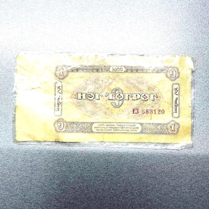 May include: A worn, rectangular banknote with text and ornate designs. The note is primarily yellow with red and brown accents. The text includes the number "1" in multiple locations, along with the year "2006" and the serial number "E3 683120".