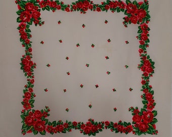 Pode incluir: Um quadrado de tecido branco com uma borda floral vermelha e verde. A borda é composta por rosas e folhas. O centro do tecido é branco liso.