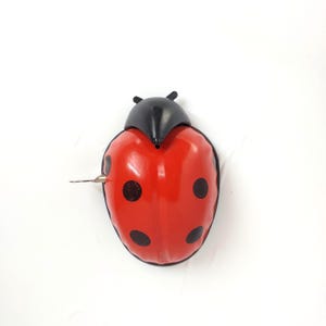 May include: A red ladybug wind-up toy with black spots and a black head. The toy has a metal winding key on its side. The ladybug is a classic toy design.