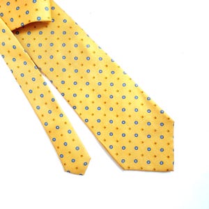 May include: A yellow tie with a repeating pattern of blue circles and small brown squares. The tie is made of a smooth fabric and is displayed on a white background. The tie is a classic accessory for formal or business attire.