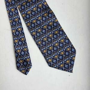 May include: Navy blue tie with a repeating pattern of gold and light blue floral designs. The tie is made of a smooth fabric and is suitable for formal or business attire.