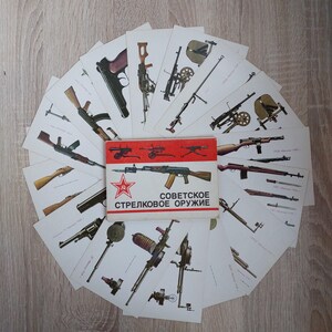 May include: A collection of vintage postcards featuring illustrations of Soviet small arms. The postcards are arranged in a fan shape, with a red and white booklet titled "Soviet Small Arms" in the center. The booklet features a red star and illustrations of various weapons.