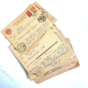 May include: A stack of vintage postcards with handwritten text, stamps, and postmarks. The postcards are in various shades of tan and beige, with text in a foreign language. The postcards are stacked on top of each other.