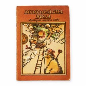 Pode incluir: Um livro vintage com capa laranja queimado apresentando o título "МОЛОДИЛЬНА ВОДА" e "українська народна казка". A ilustração retrata um veleiro, uma pessoa tocando flauta, um gato usando chapéu e pequenos roedores em estilo desenhado.