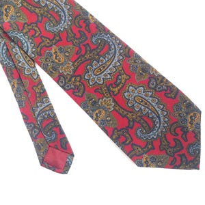 May include: A red paisley tie featuring a detailed pattern in blue, yellow, and gold. The tie is made of a smooth fabric and is set against a white background. The classic design is suitable for formal or business wear.