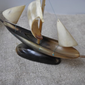May include: A small, handcrafted sailboat made from horn. The sails are white and the hull is dark brown. The boat is sitting on a dark brown base.