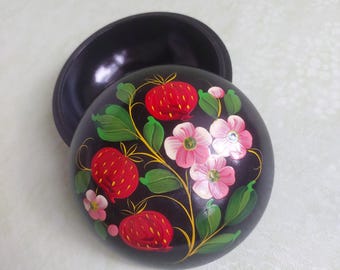 May include: A black wooden trinket box with a round lid. The lid is painted with a floral design featuring red strawberries, pink flowers, and green leaves.
