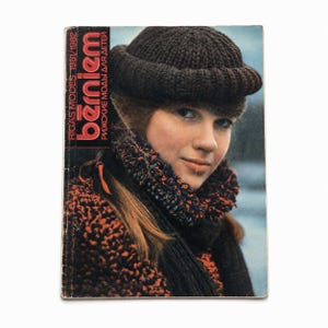 May include: A vintage 1981/1982 Rīgas Modes bērniem magazine cover featuring a person wearing a dark brown knit beanie and a textured, multi-colored scarf with orange and black tones. The cover includes the text Rīgas Modes 1981/1982 bērniem.