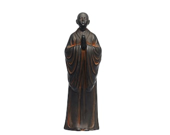 May include: A black and brown figurine of a person in a robe with their hands clasped in prayer.