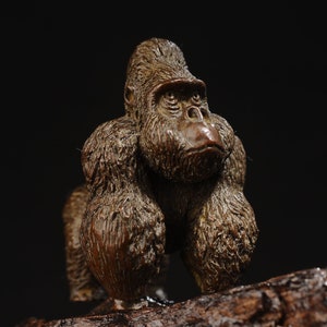 Op de afbeelding: Een gedetailleerd bronzen beeld van een gorilla, staand op een houten voet. De gorilla is afgebeeld met een realistische, getextureerde vacht en een serieuze uitdrukking.